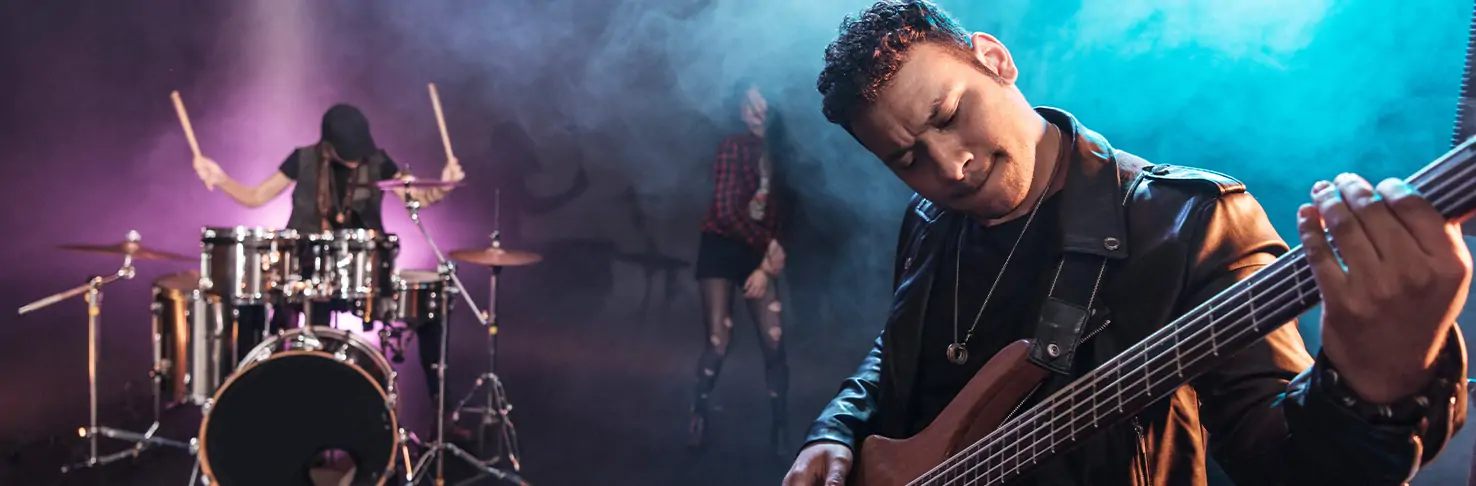 A dynamic band performs safely on a secure stage setup in Panama City, Florida, showcasing a focused bass player in the foreground, with a blurred drummer and a vocalist in the background, all enveloped in atmospheric stage lighting and haze that highlights the professional and secure ambiance of the event staging.