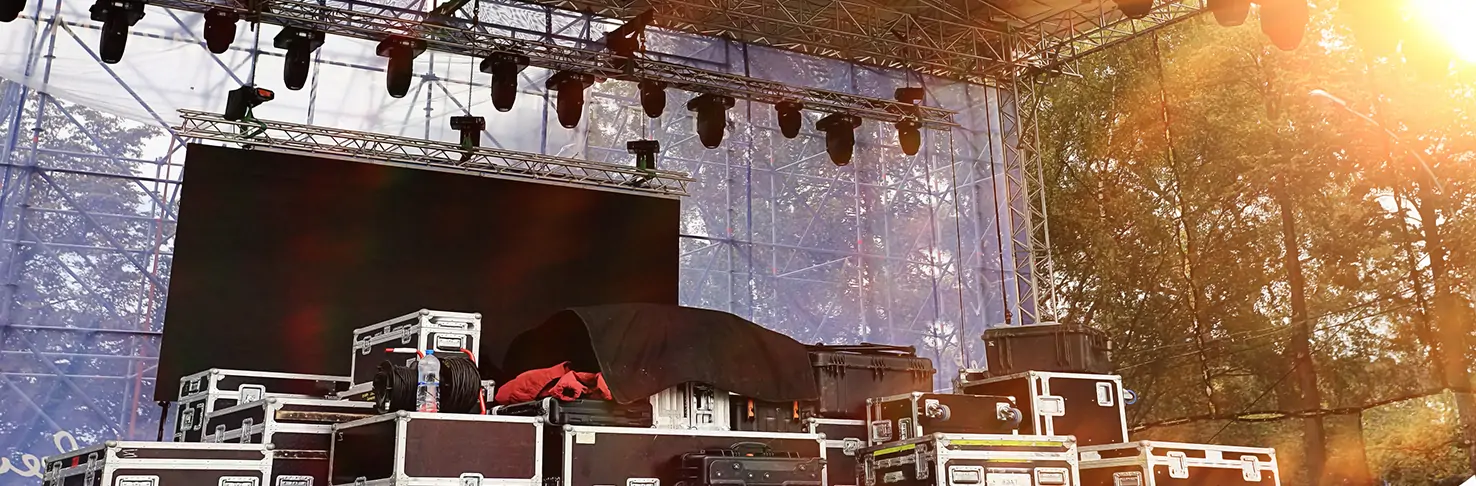 A robust outdoor stage set up in Panama City, Florida, bathed in the golden glow of the setting sun. The stage is equipped with professional audio and lighting equipment, secured on top of sturdy staging platforms, surrounded by flight cases used for safe equipment transport. This scene exemplifies the reliable and comprehensive event production services offered in the area, ready for a transformative performance.